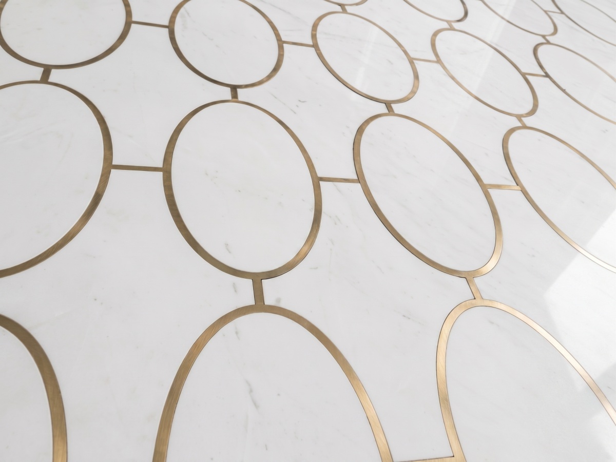Close-up of white marble flooring with subtle grey veining and brass-colored inlay for a casino project
